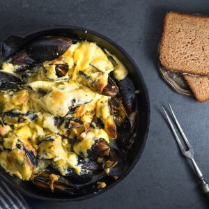 Mussels with cheese sauce in a frying pan, bread on a saucer, fork